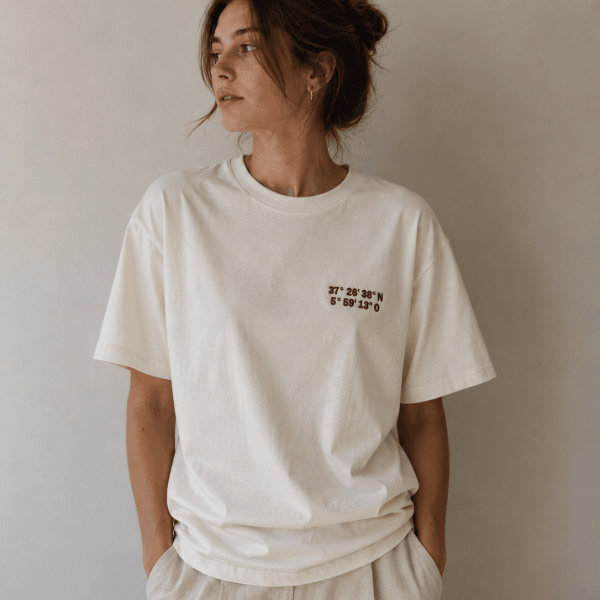 Mujer con camiseta marfil de Acusmagna. con bordado de coordenadas en color granate elegante.